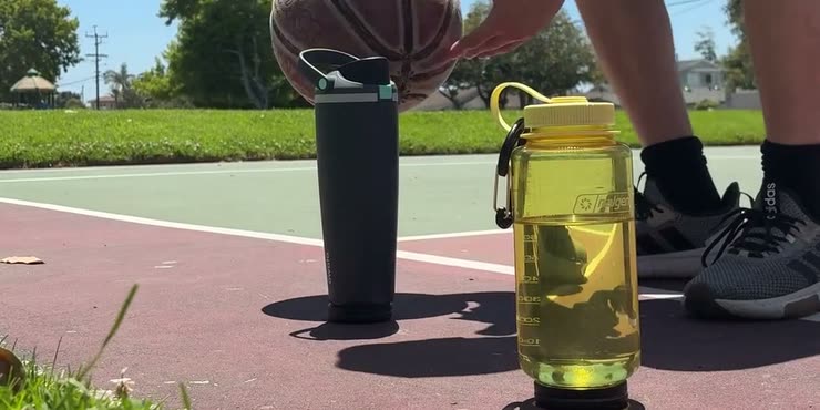 Two water bottles with Sponge trackers clipped to their bases on an outdoor basketball court